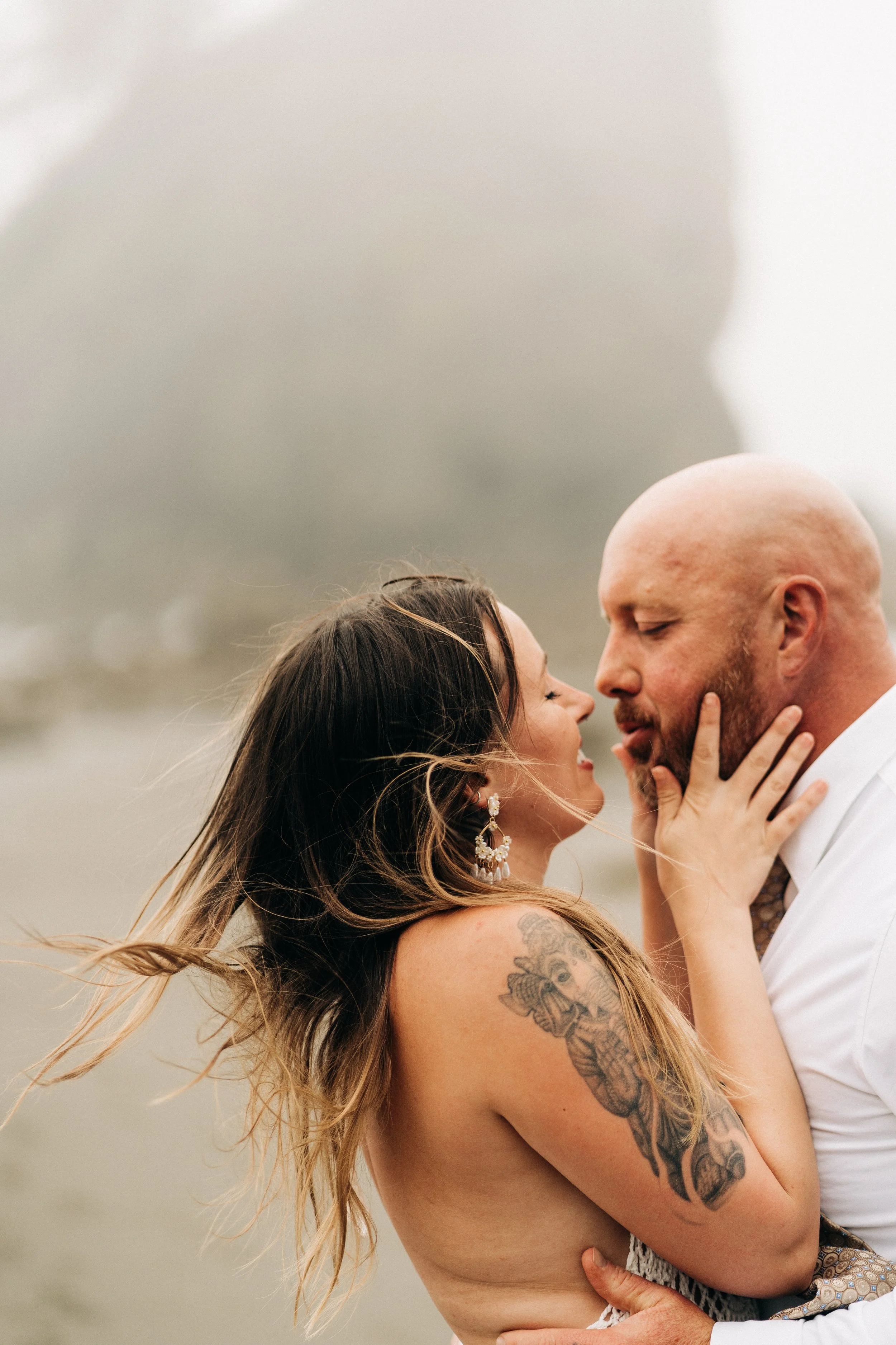 A couple is kissing outdoors on a foggy day, with the woman holding the man's face and the man embracing her.
