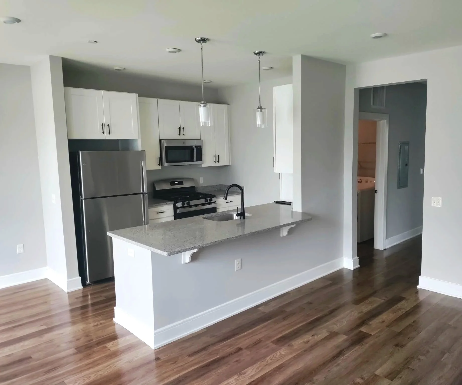 Modern kitchen with white cabinets, stainless steel appliances, a granite island with a sink, pendant lights, and hardwood flooring.
