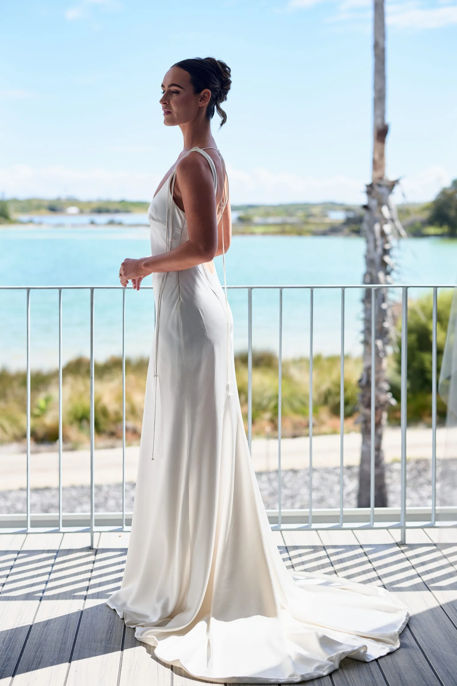 A bride in a long white gown on a deck above the lake