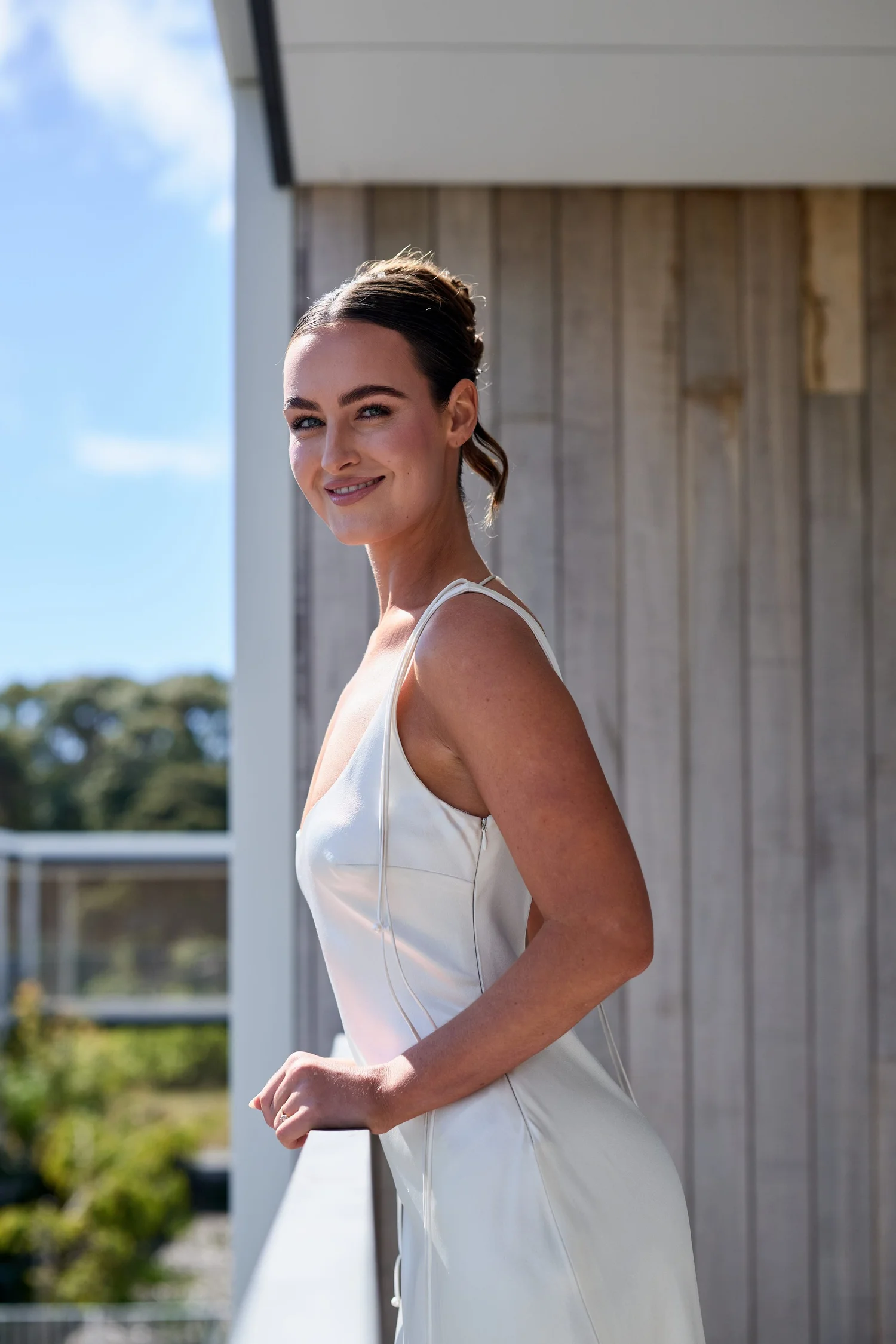 A smiling bride in a white gown on a balcony