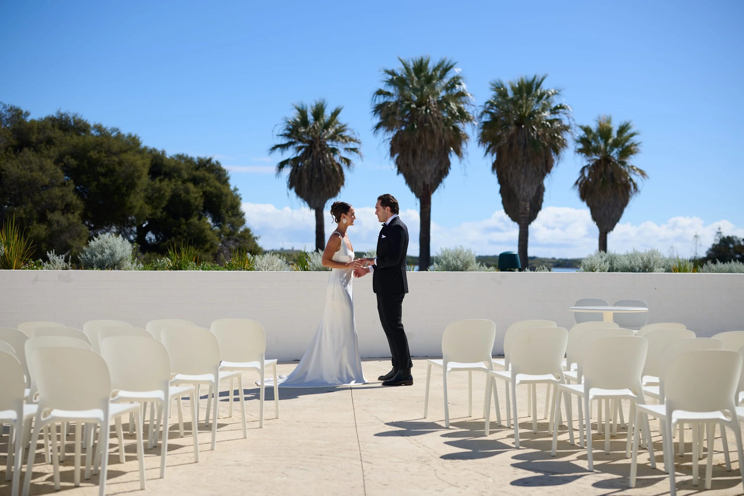 White chairs set for a ceremony at the Gathering Ground, with palms and open sky beyond