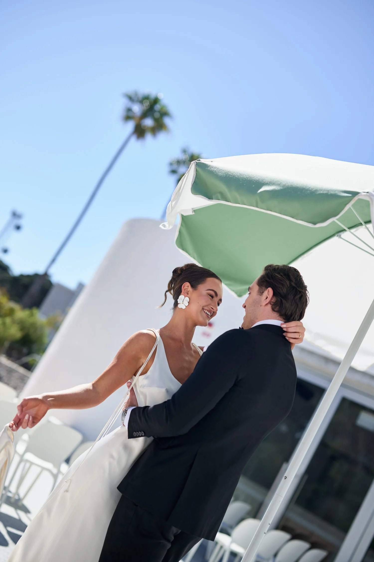 A couple embracing beside white chairs and a green and white umbrella