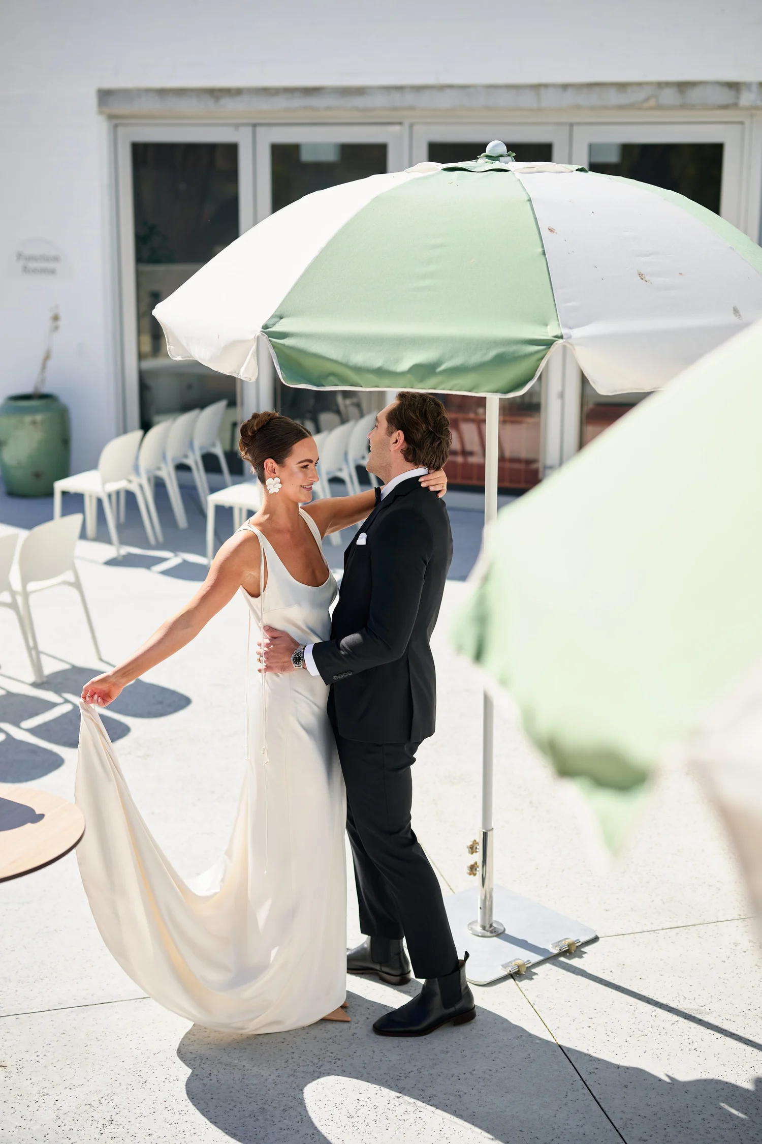 A couple embracing beside white ceremony chairs and a green and white umbrella