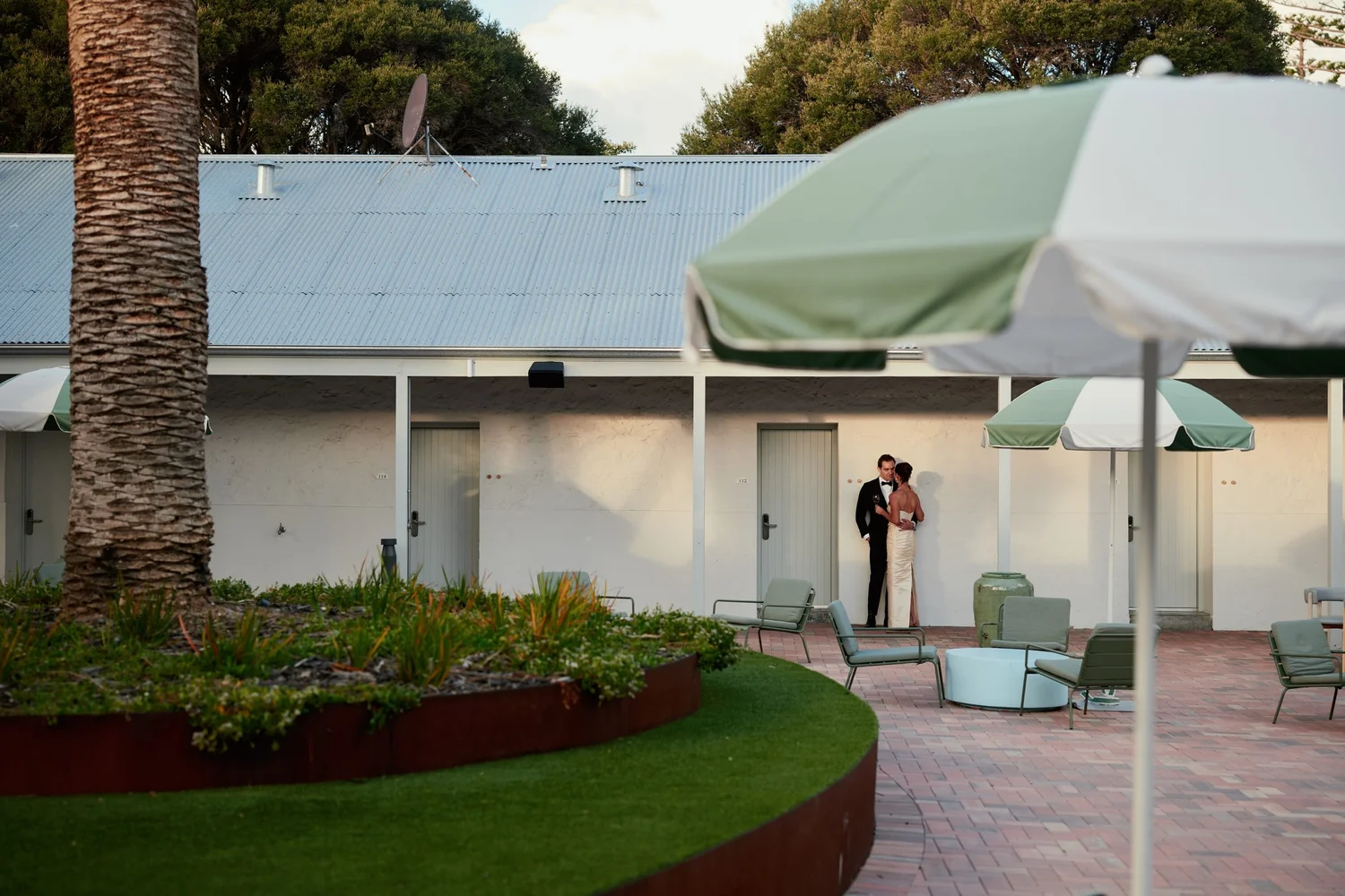 The Courtyard at The Lodge, with lawn, palm, umbrellas and outdoor seating