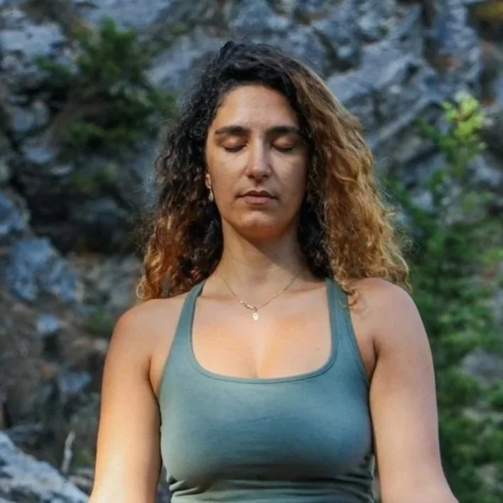 Woman meditating with eyes closed with trees and rock in the background.