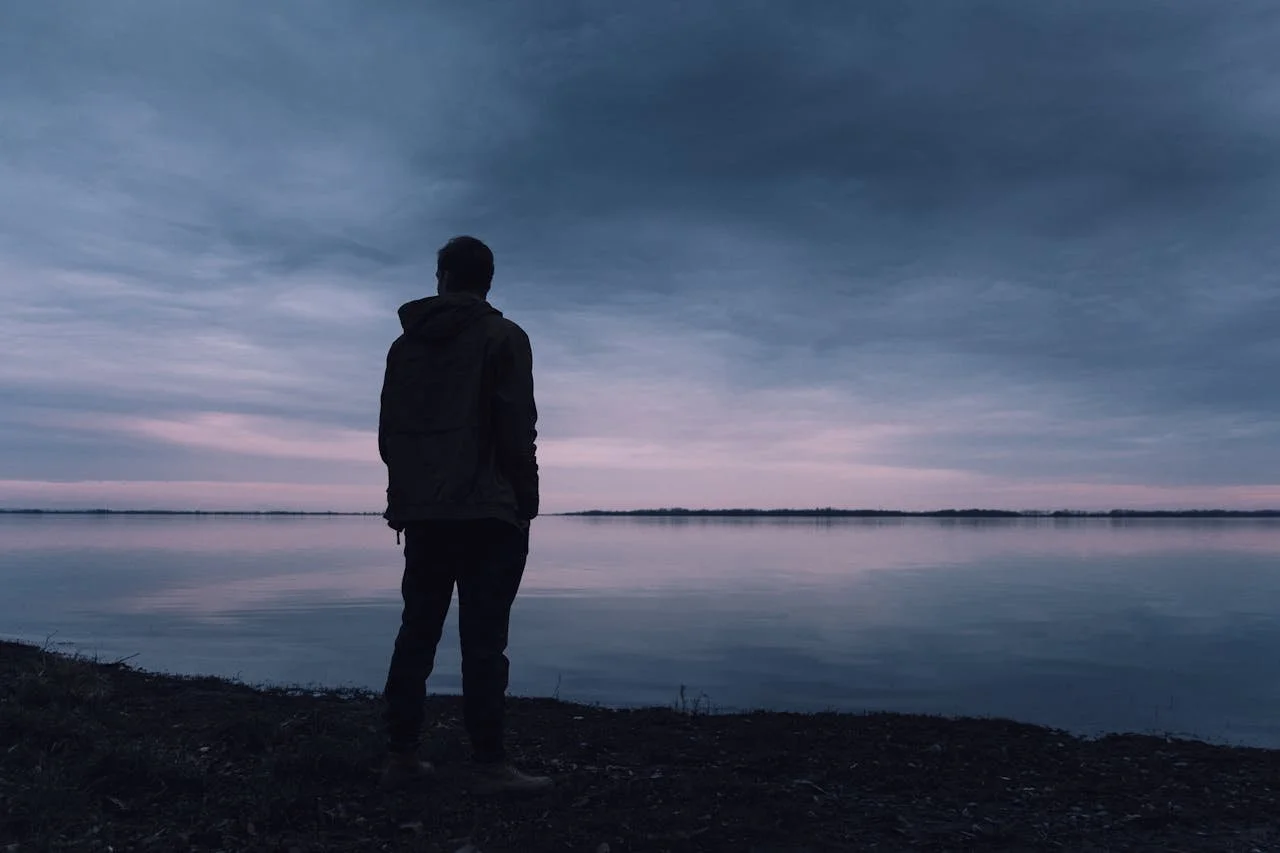 Man wearing a coat looking out over a lake at dusk.