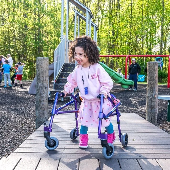 A young girl uses her walker on the ramp of the wheelchair accessible playground structure.