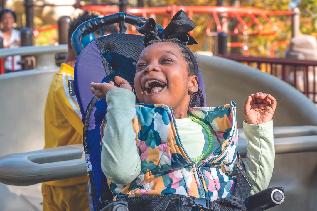 A little girl seated in a wheelchair is expressing her delight