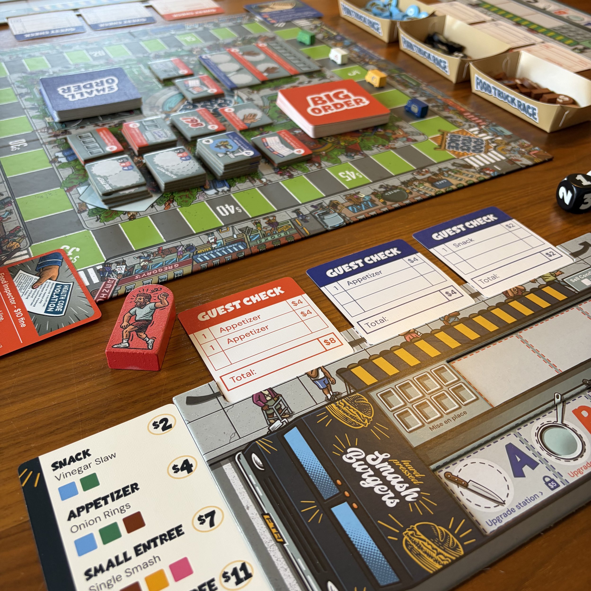 Close-up of a board game in progress with game pieces, cards, and paper score sheets on a wooden table, including game components like guest check cards for food orders and a menu with snack and appetizer options.