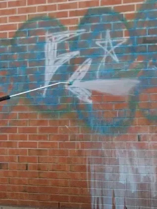 Graffiti being removed by pressure washing machine nozel.