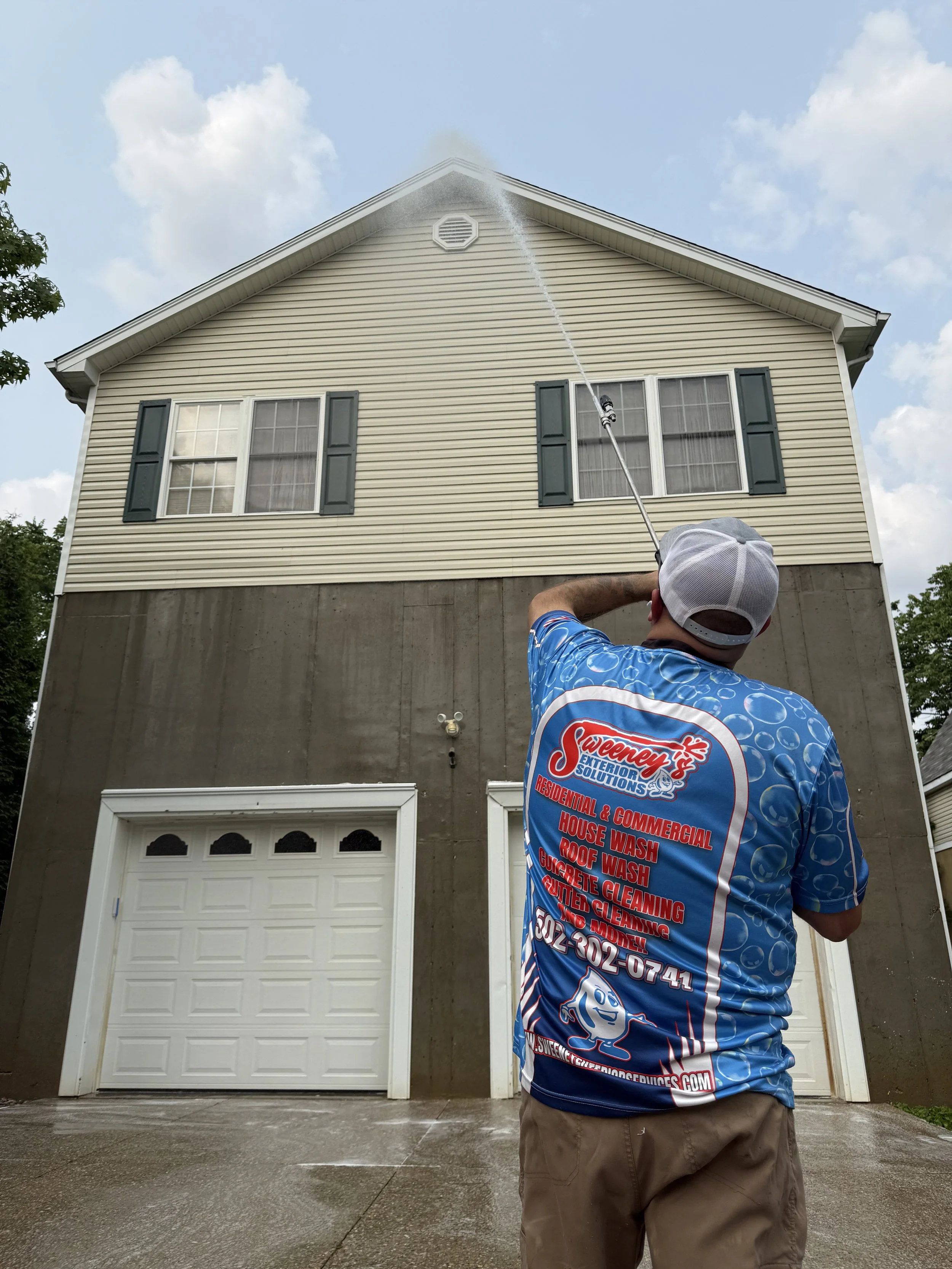 Sweeney's Exterior Solutions owner Ryan Sweeney cleaning the upper exterior of a two-story house with a pressure washer.
