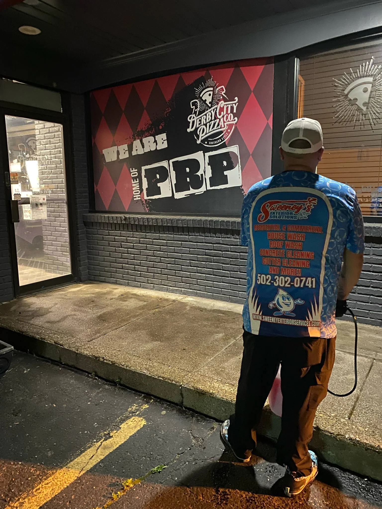 Night view of Sweeney's Exterior Solutions owner Ryan Sweeney safely pressure washing the exterior of Derby City Pizza Co. restaurant in Louisville, KY.