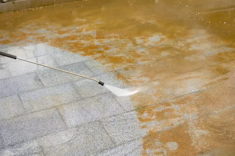 Power washer cleaning a stained brick or concrete surface outdoors.