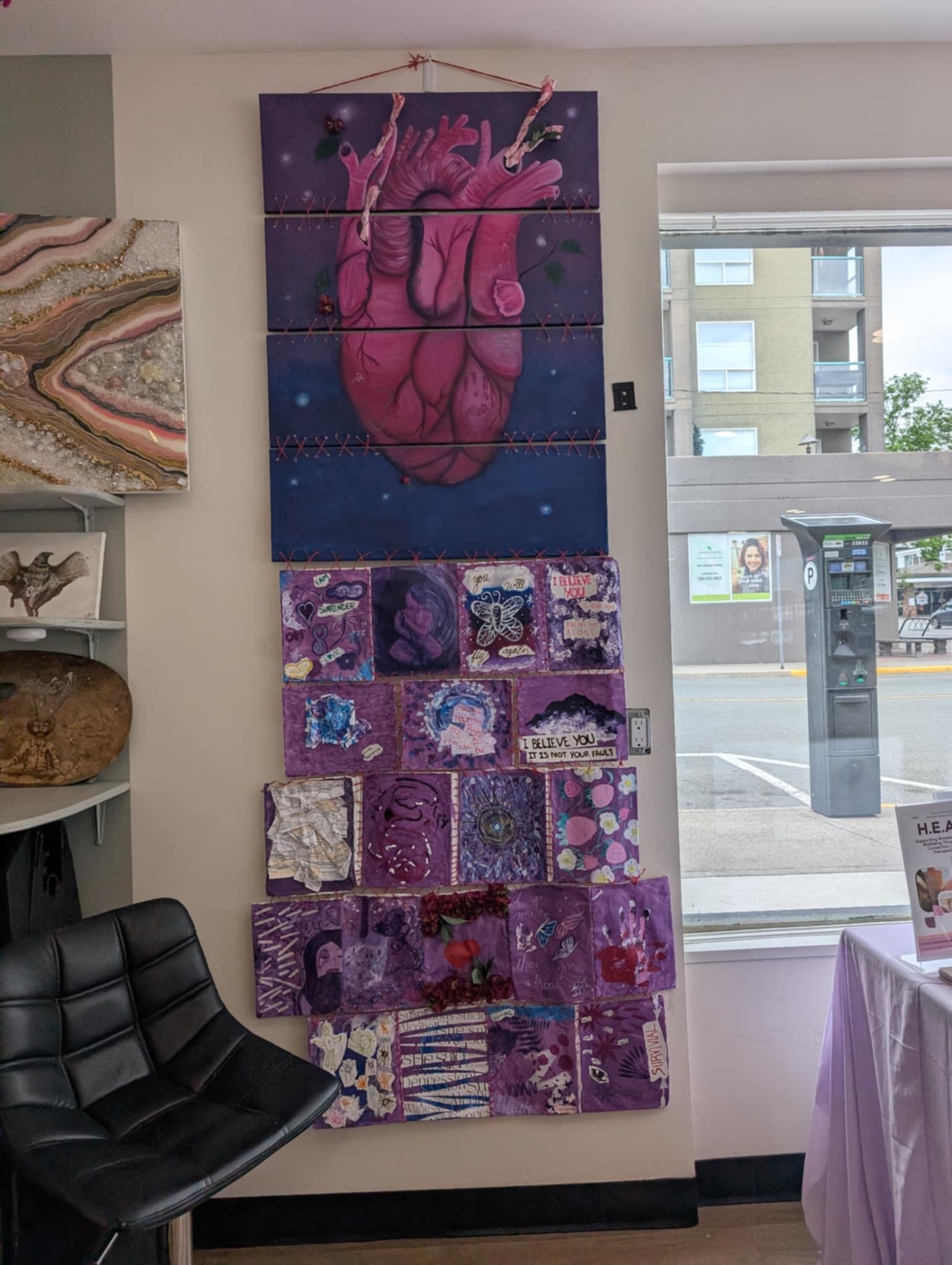 A series of art pieces on a wall, with a large painted anatomical heart at the top, followed by a collage of smaller artworks below, all predominantly in purple hues.