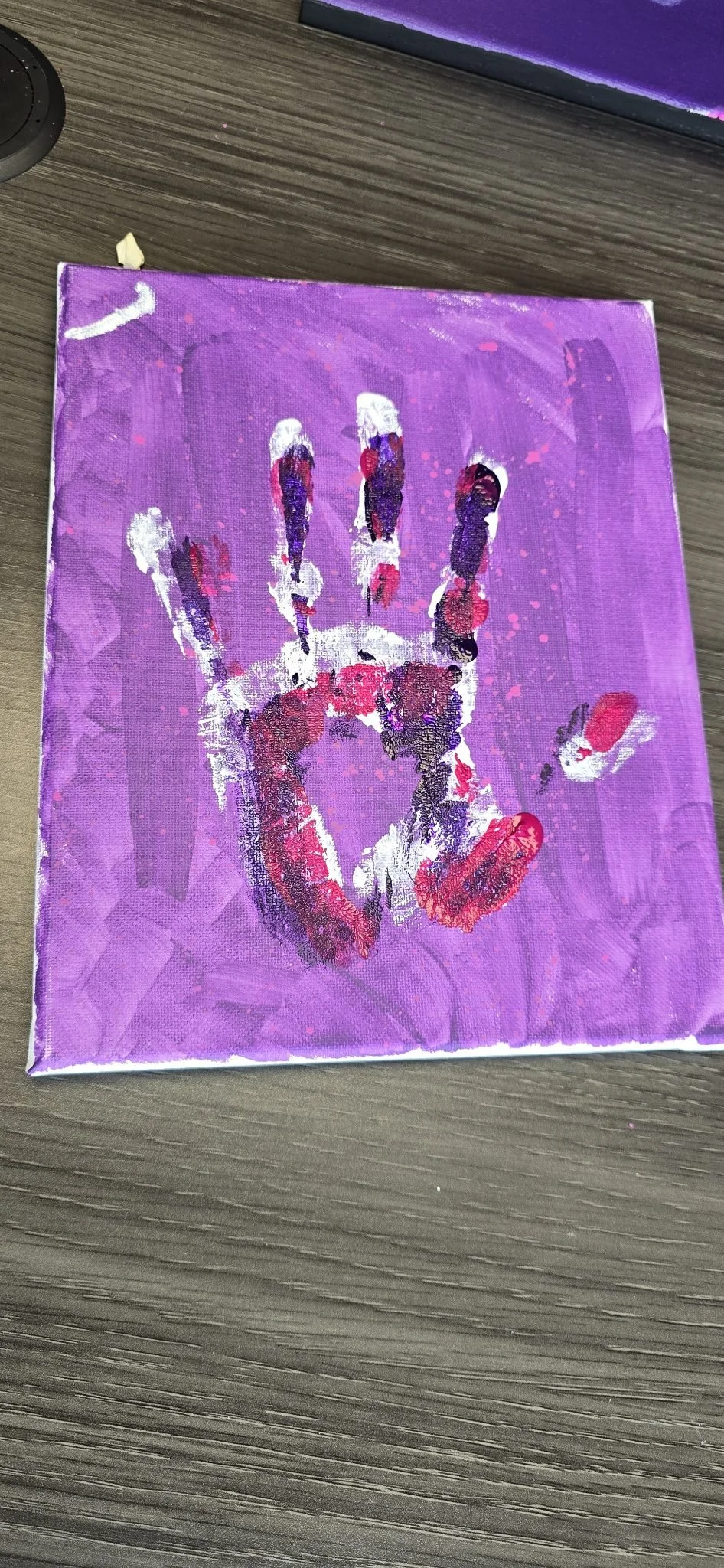 Painted handprint on purple canvas with pink, white, and dark purple colors.