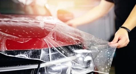 Persona colocando una lámina protectora en un auto rojo.