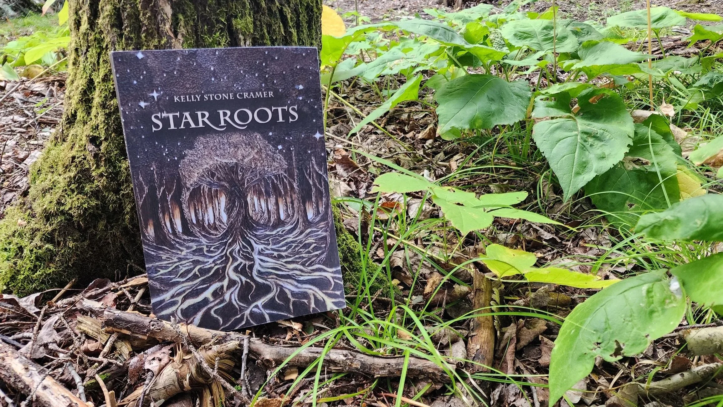 A book titled "Star Roots" by Kelly Stone Cramer. A red and white banner across the book reads "Coming Soon!" This is a mythic fantasy following a celestial guardian who must embrace her cosmic origins to protect the natural world.