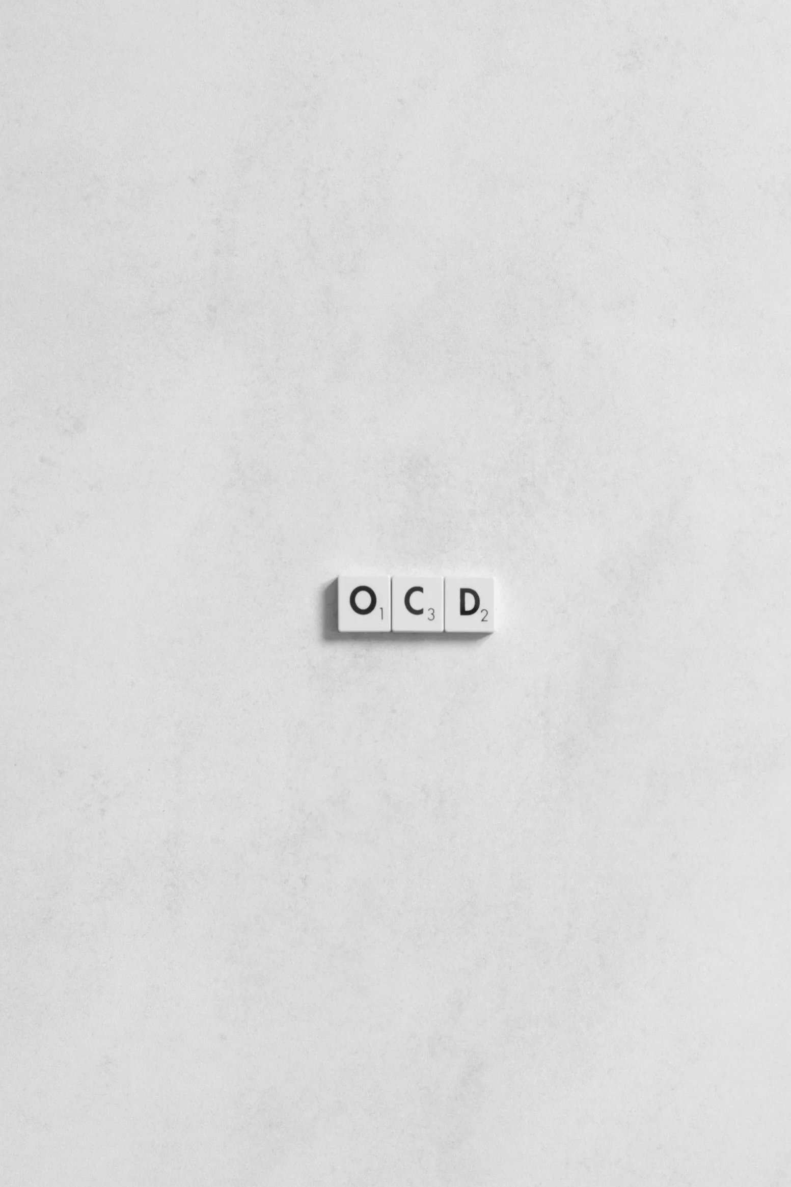 Scrabble tiles spell out 'OCD' on a white background.