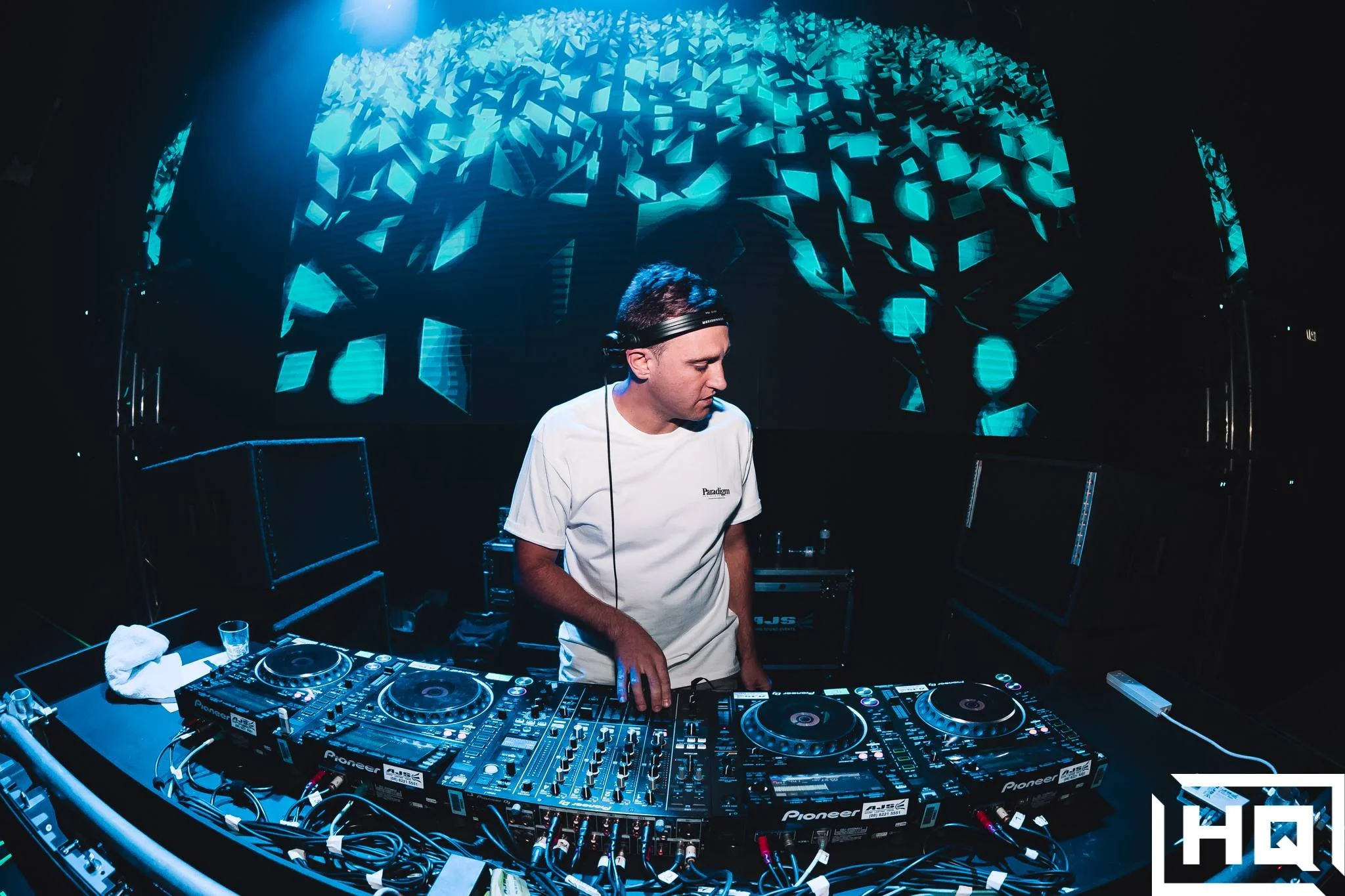 male wearing headphones and standing behind dj equipment in front of a giant LED screen with blue VFX