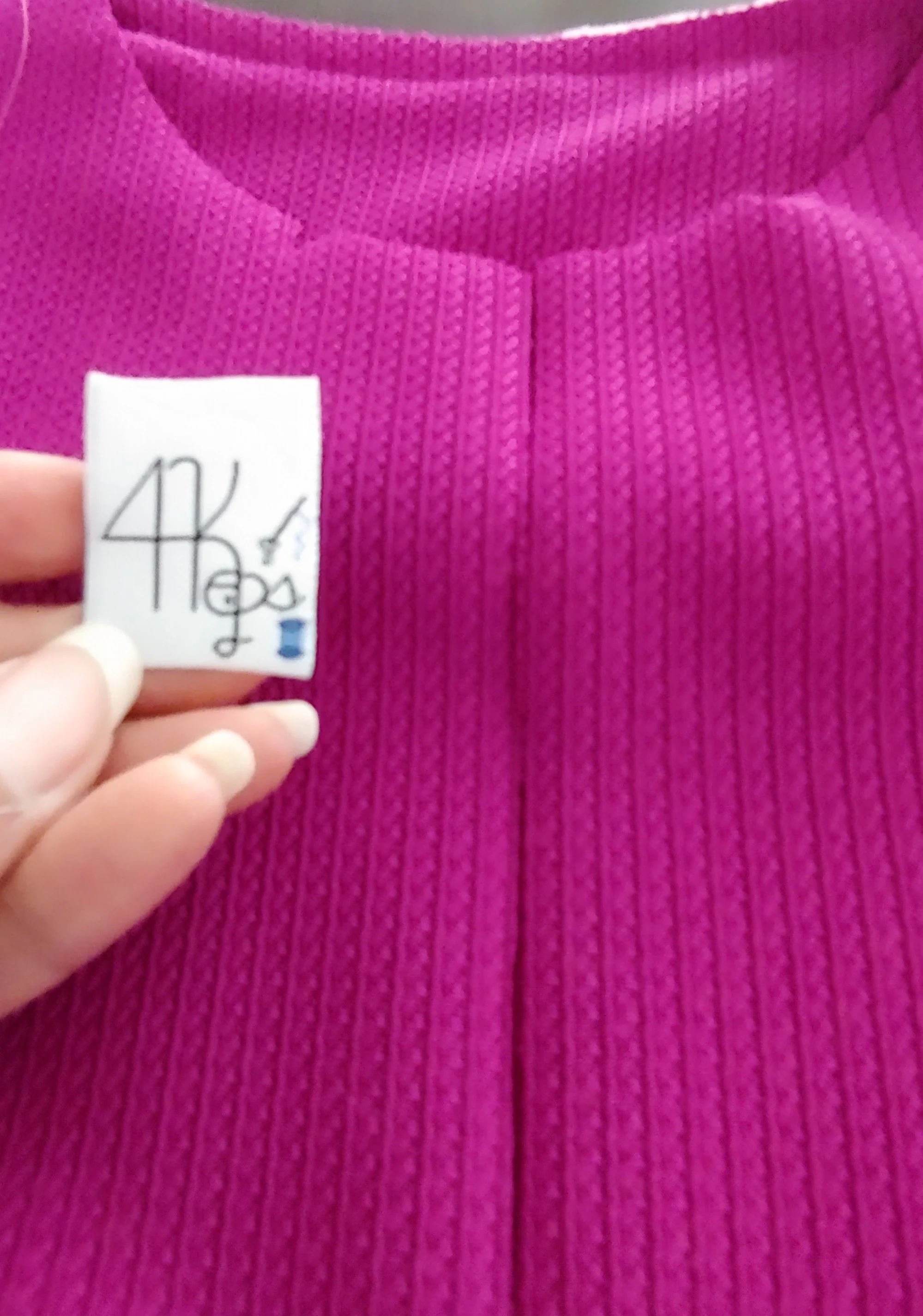 Close-up of a pink ribbed garment with a white label held by a person's hand.