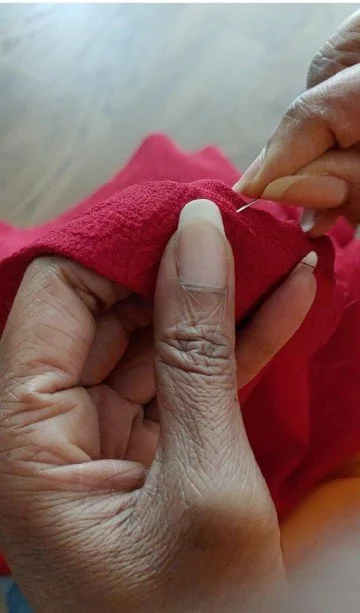 Neckline of a Red Floral Jacquard Blouse being carefully handstitched in place with a needle and thread.