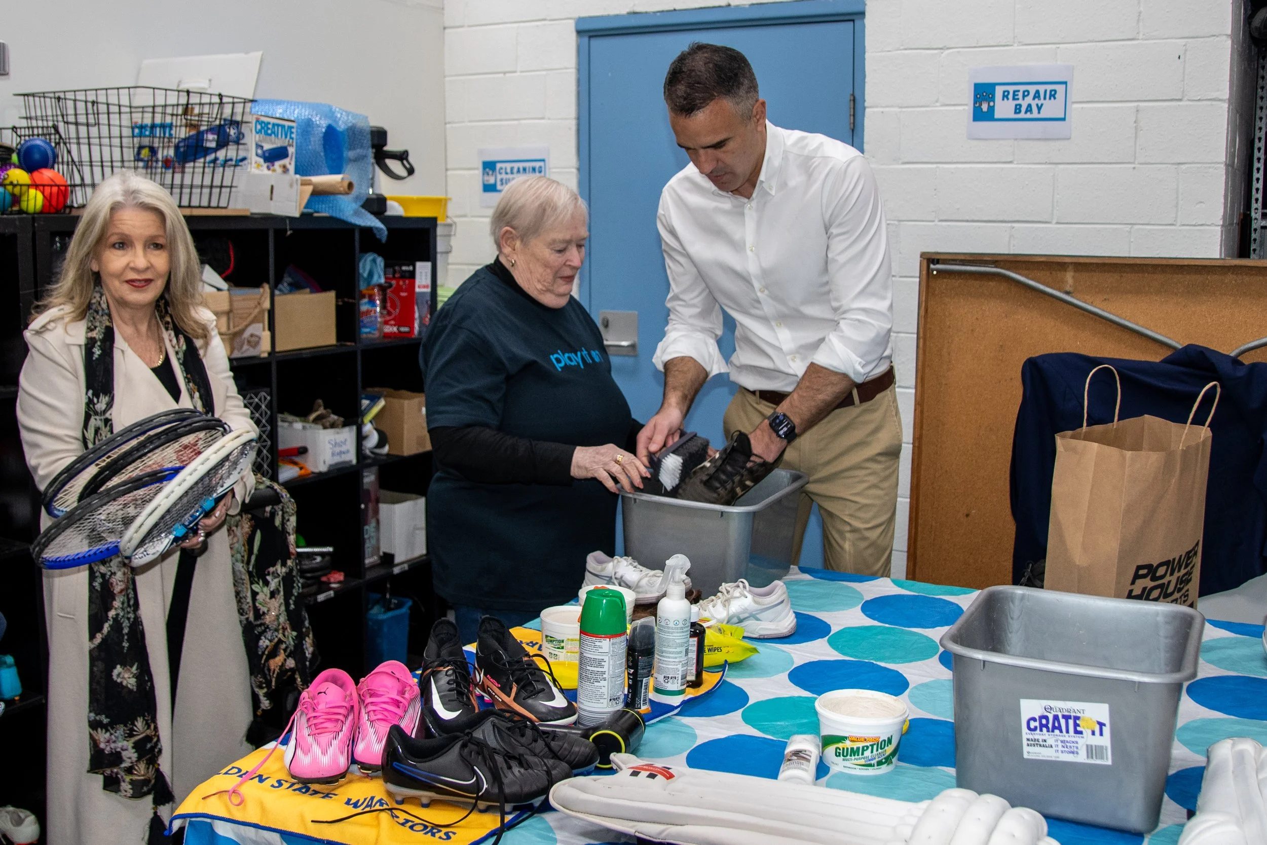 Play it On volunteer Judith teaches Peter Malinauskas how to clean footy boots at the Play It On Shop launch
