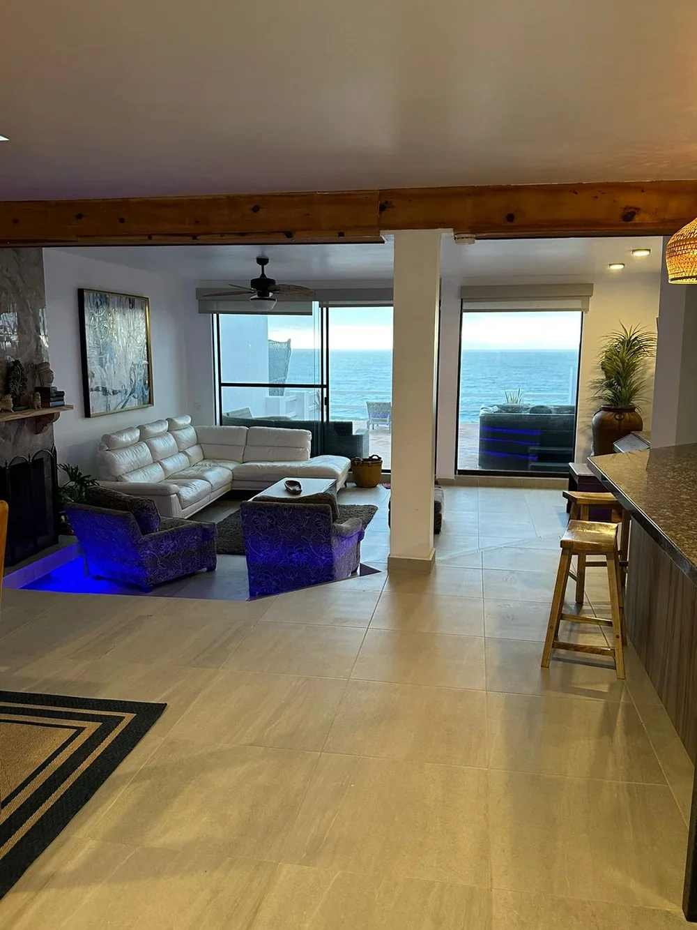 Coastal living room with large windows overlooking the ocean, white sectional sofa, purple armchairs, glass sliding doors, and beach view.