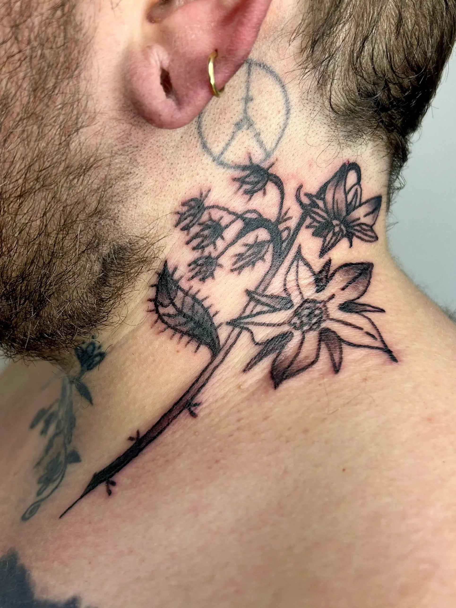 Tattoos on a person's neck and face, including a peace sign, a butterfly, and floral designs.