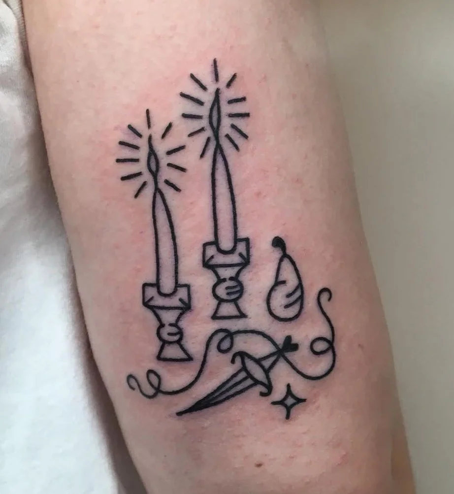 Tattoo of two lit candles with sparking flames, a pear-shaped object, a pointed pencil, and some decorative lines and sparkles.