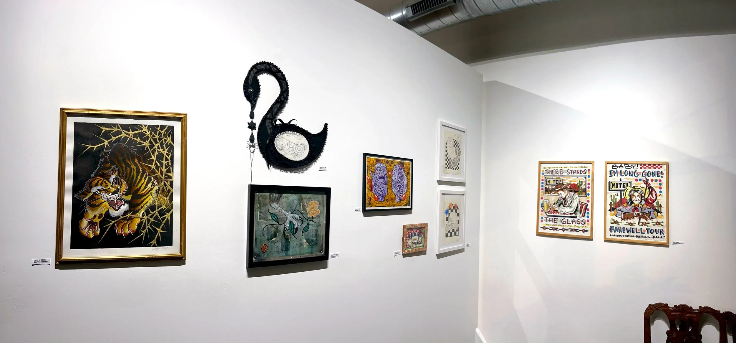 Gallery wall with various framed artwork, including a tattoo-style tiger, a black and white dragon sculpture, abstract prints, and posters with text and colorful illustrations.