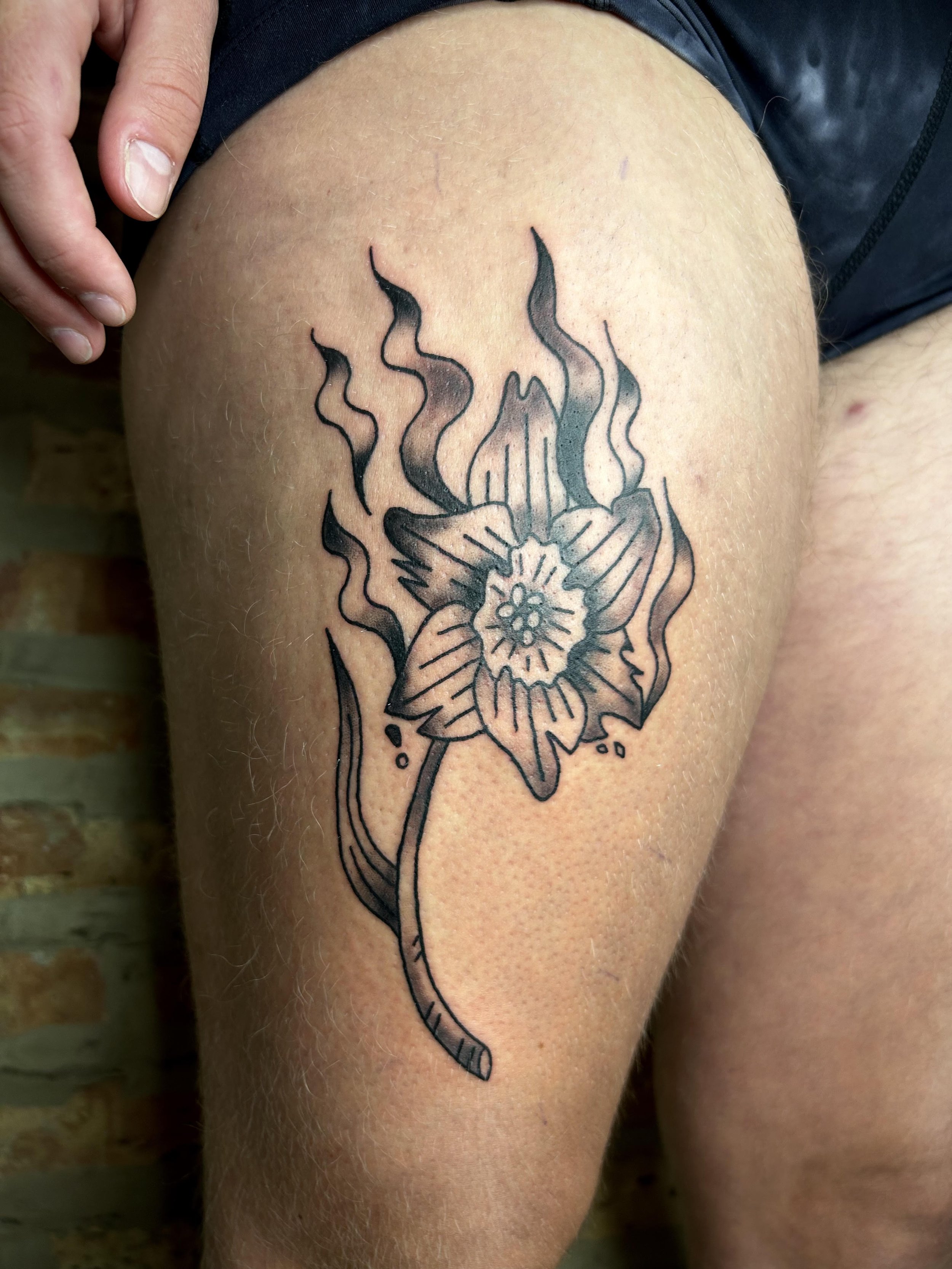 Black and gray tattoo of a flower with smoke or steam rising from it on a person's thigh.