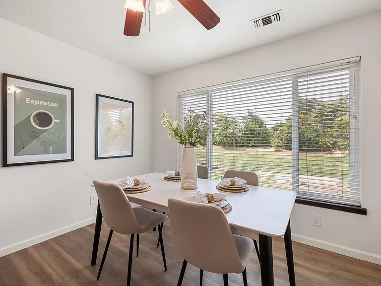 Open-concept living room and kitchen with white walls, beige tiled floors, white cabinetry, sitting area with a white sofa, framed wall art, coffee table, and dining table with five chairs.
