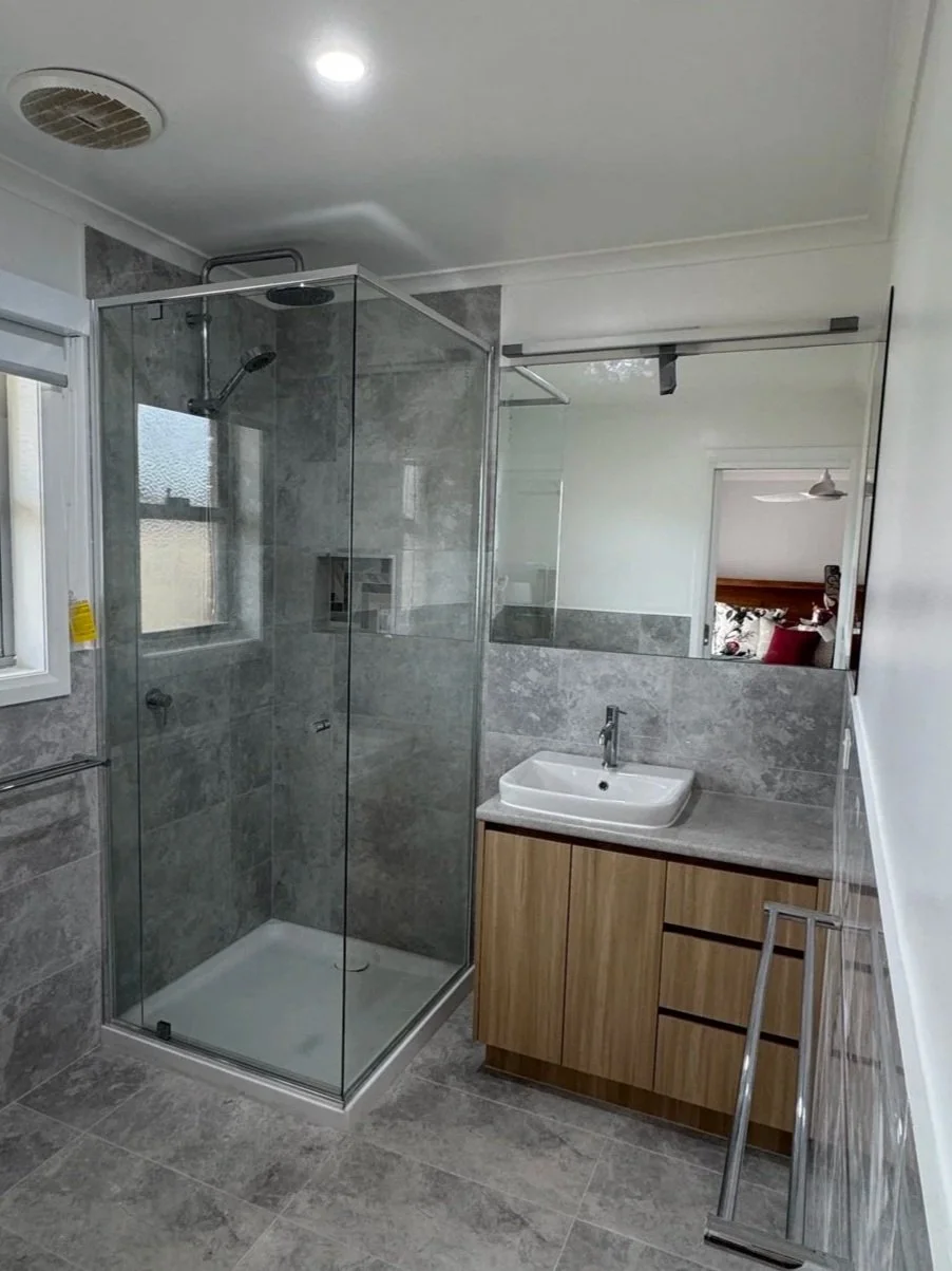 Modern bathroom with a glass-enclosed shower, a white sink on a wooden cabinet, and a large mirror on the wall.