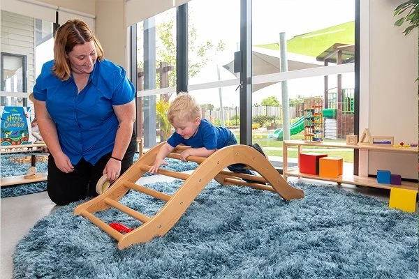 Educator helps baby over climbing frame at Highfields Central Early Learning Centre