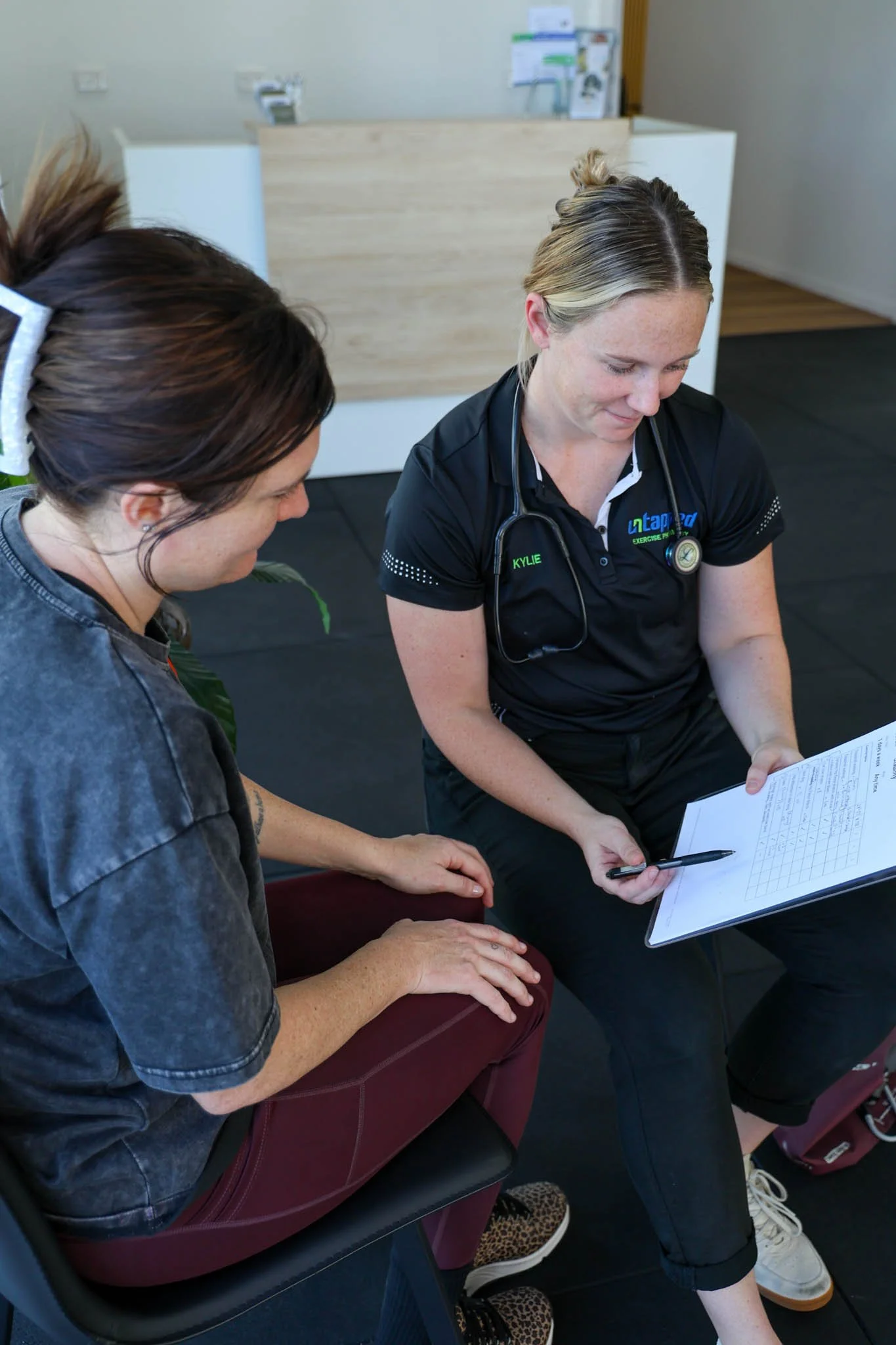 A healthcare professional and a patient seated in a clinic or hospital waiting area, reviewing medical documents and discussing patient care.