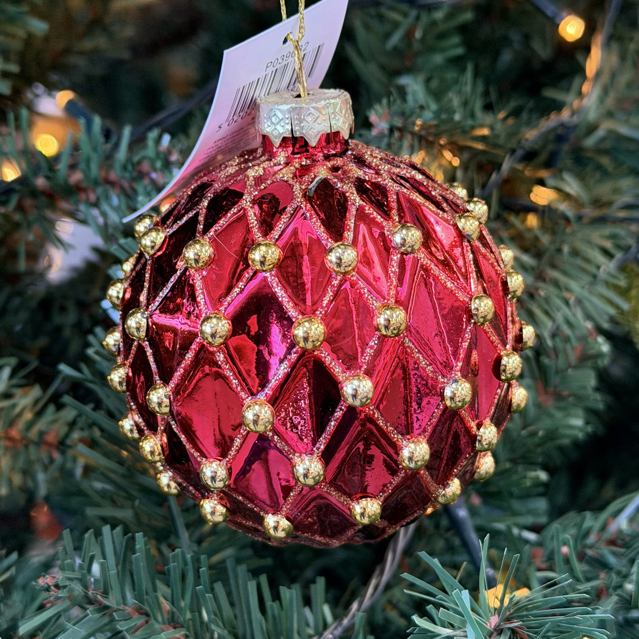 A red and gold Christmas ornament hanging on a Christmas tree with green needles.