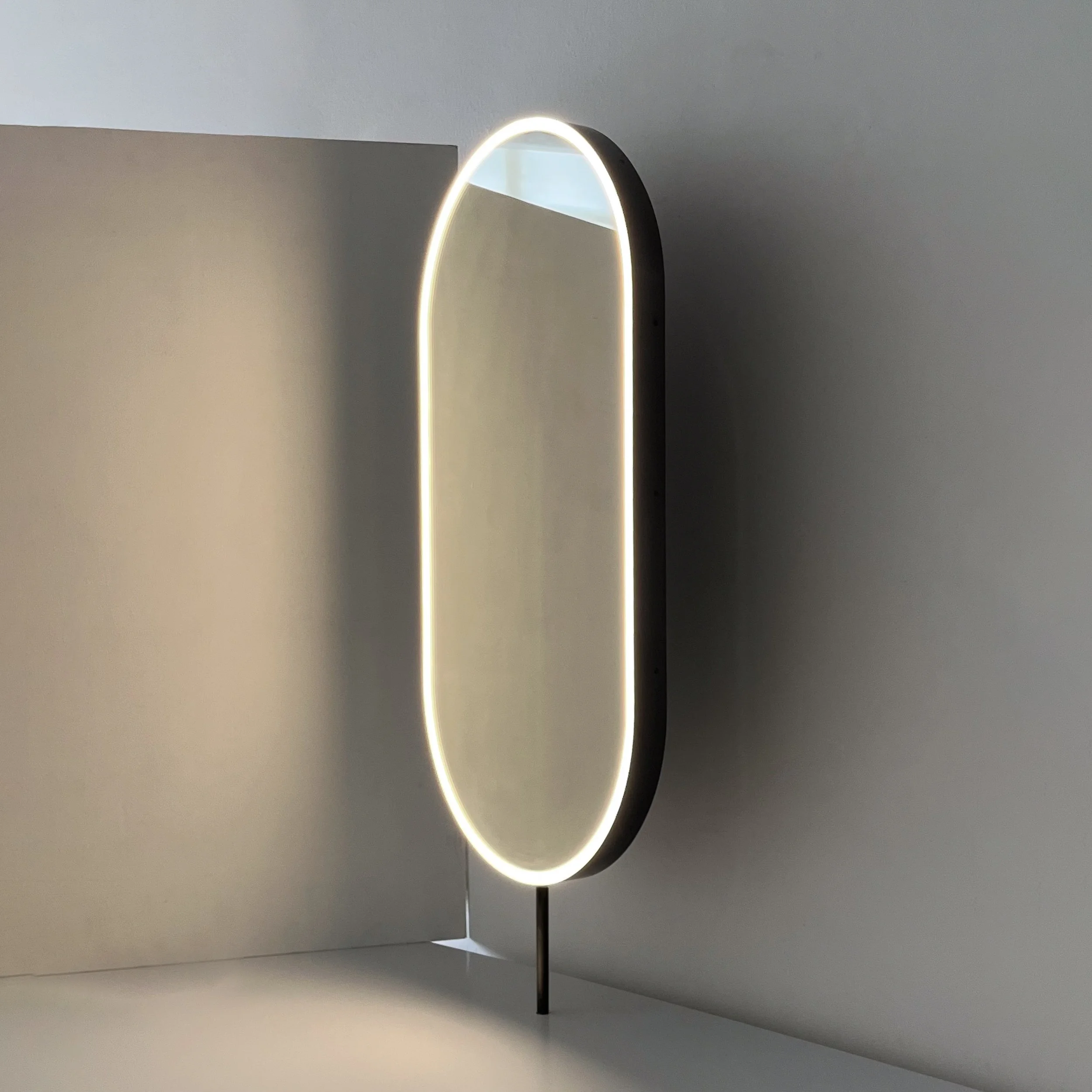 Oval-shaped  countertop mirror with LED lighting against a wall