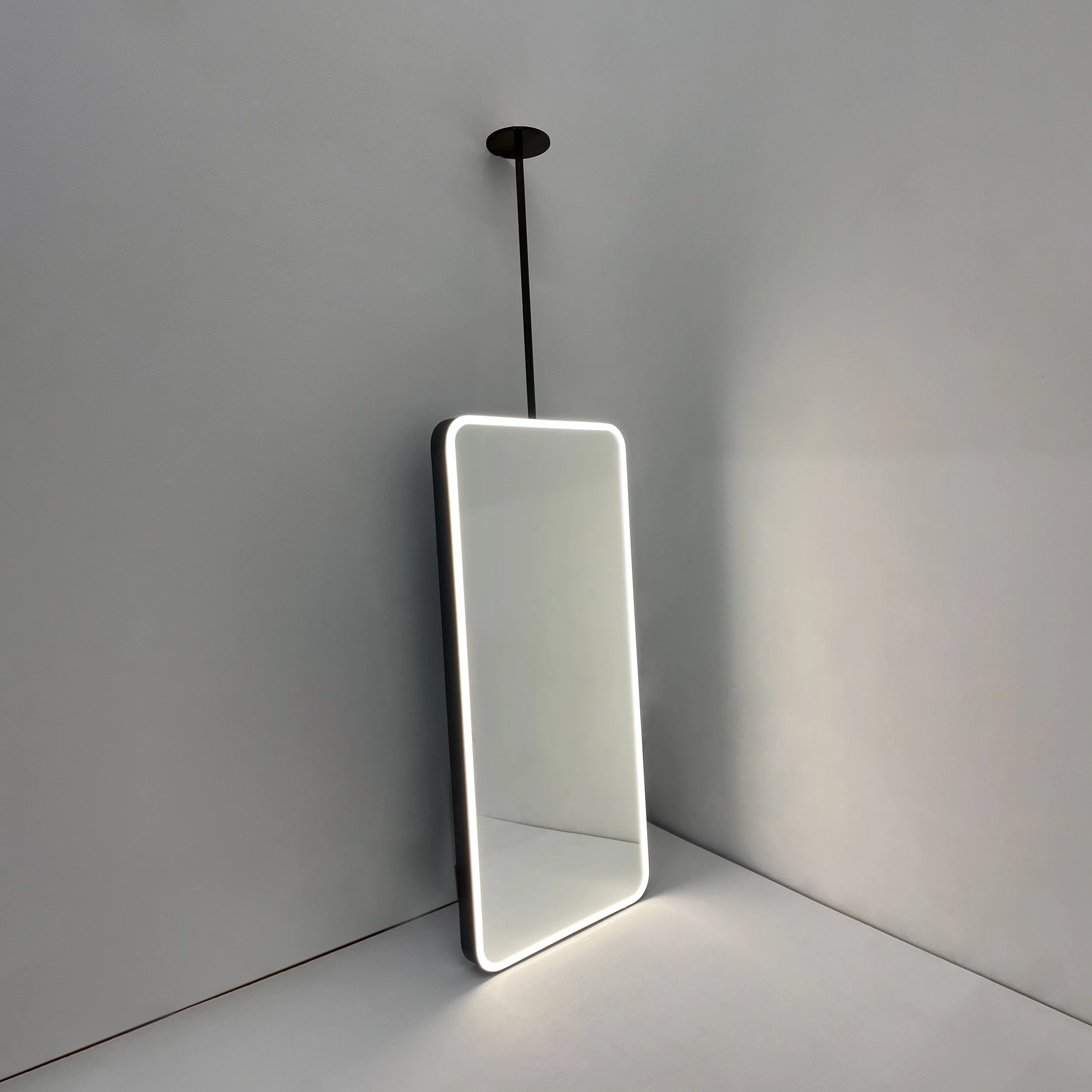 Rectangular ceiling suspended mirror with curved edges and LED illumination against a white wall.