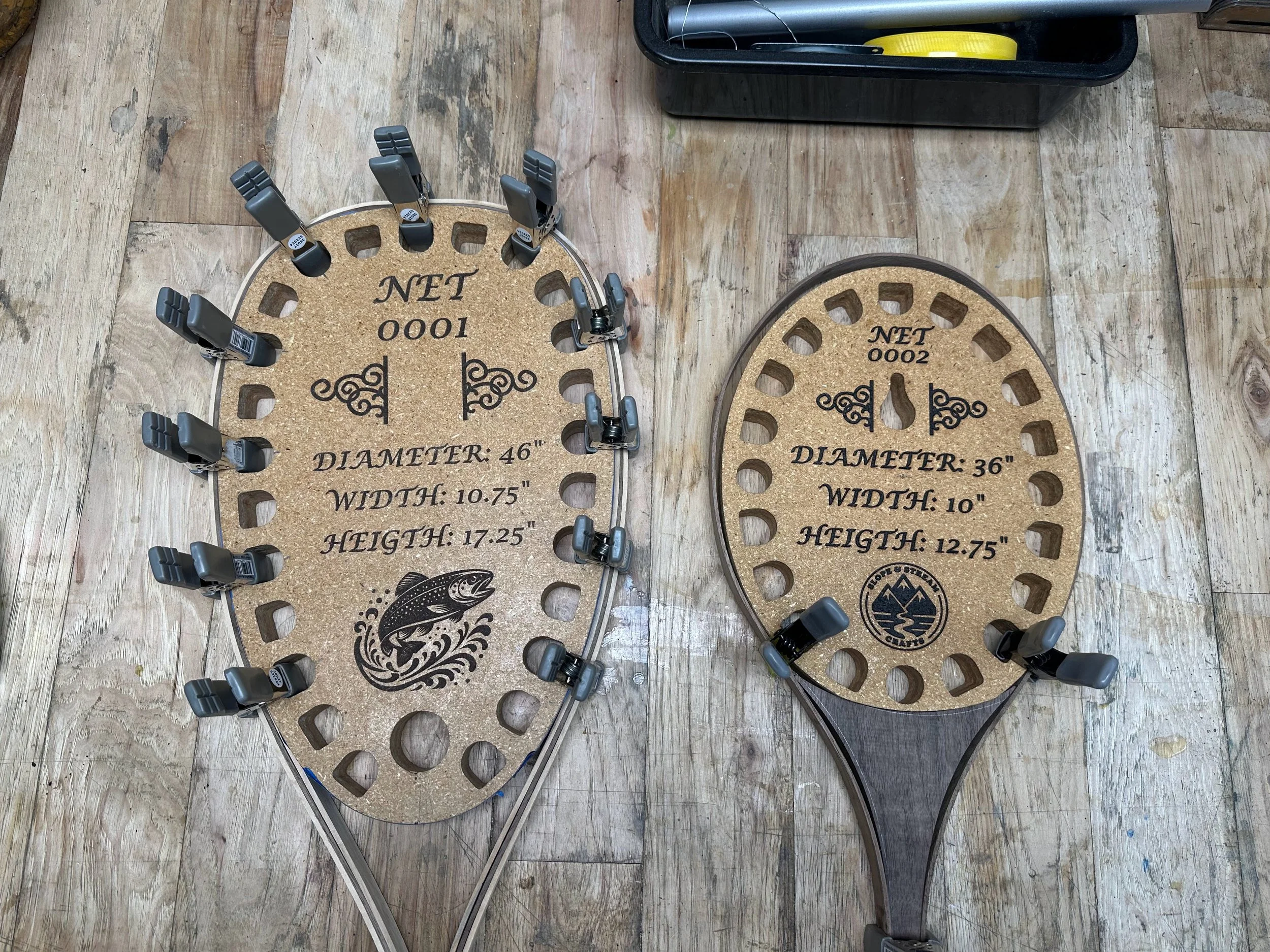 Two large cork fishing tackle boards with measurements and designs, surrounded by fishing clips, on a wooden floor. One board has the text 'NET 1000' and 'DIAMETER: 46''' and the other has 'NET 2000' and 'DIAMETER: 36'''.