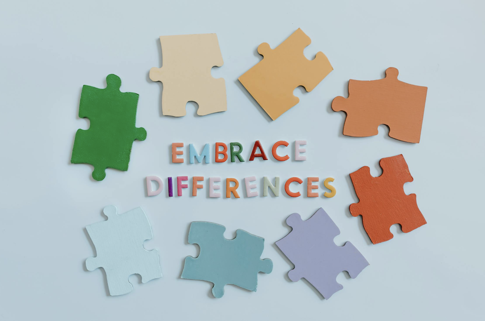 Colorful puzzle pieces and the words 'Embrace Differences' arranged on a light background.