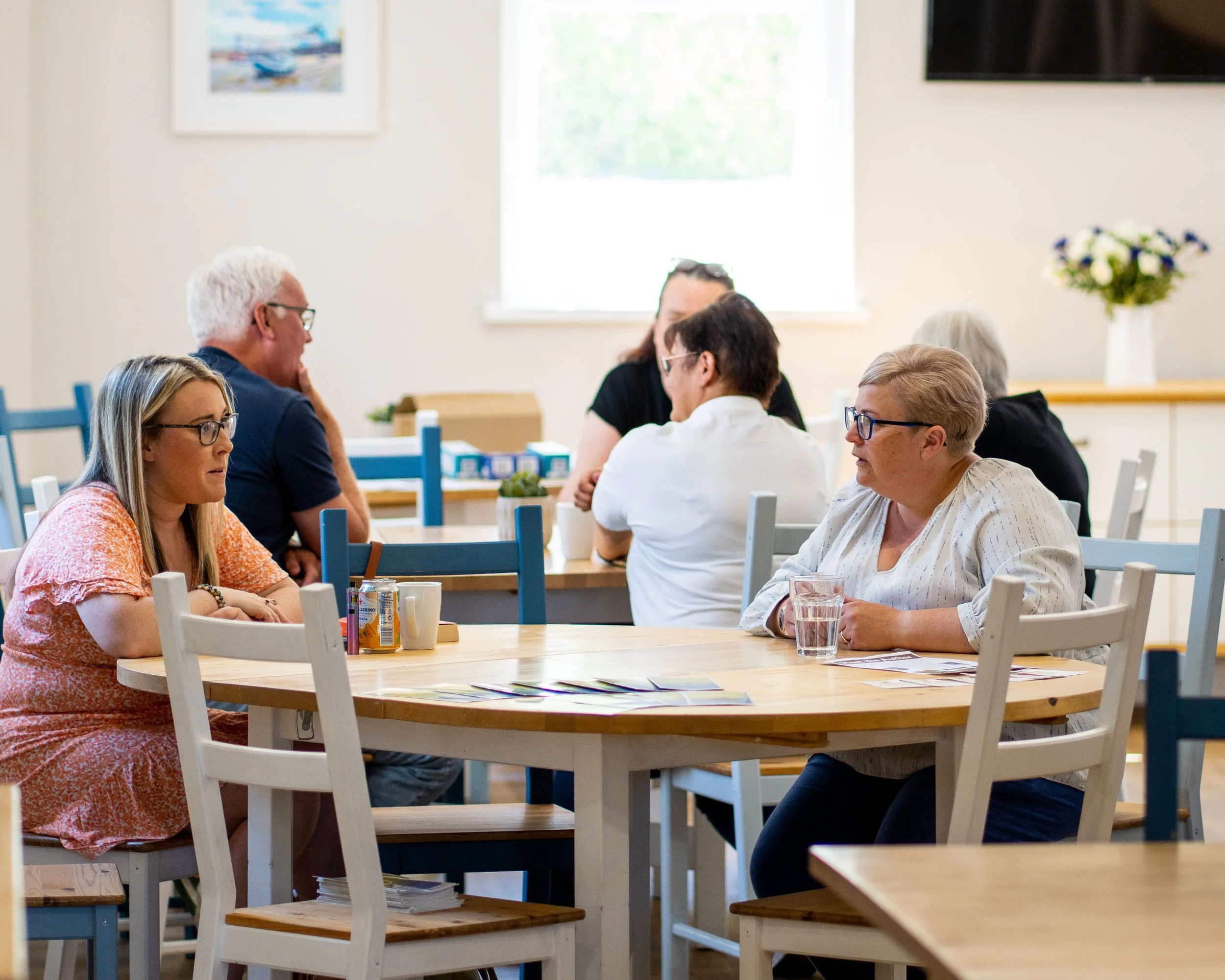 Group of people sitting at tables in a room, engaged in conversation.