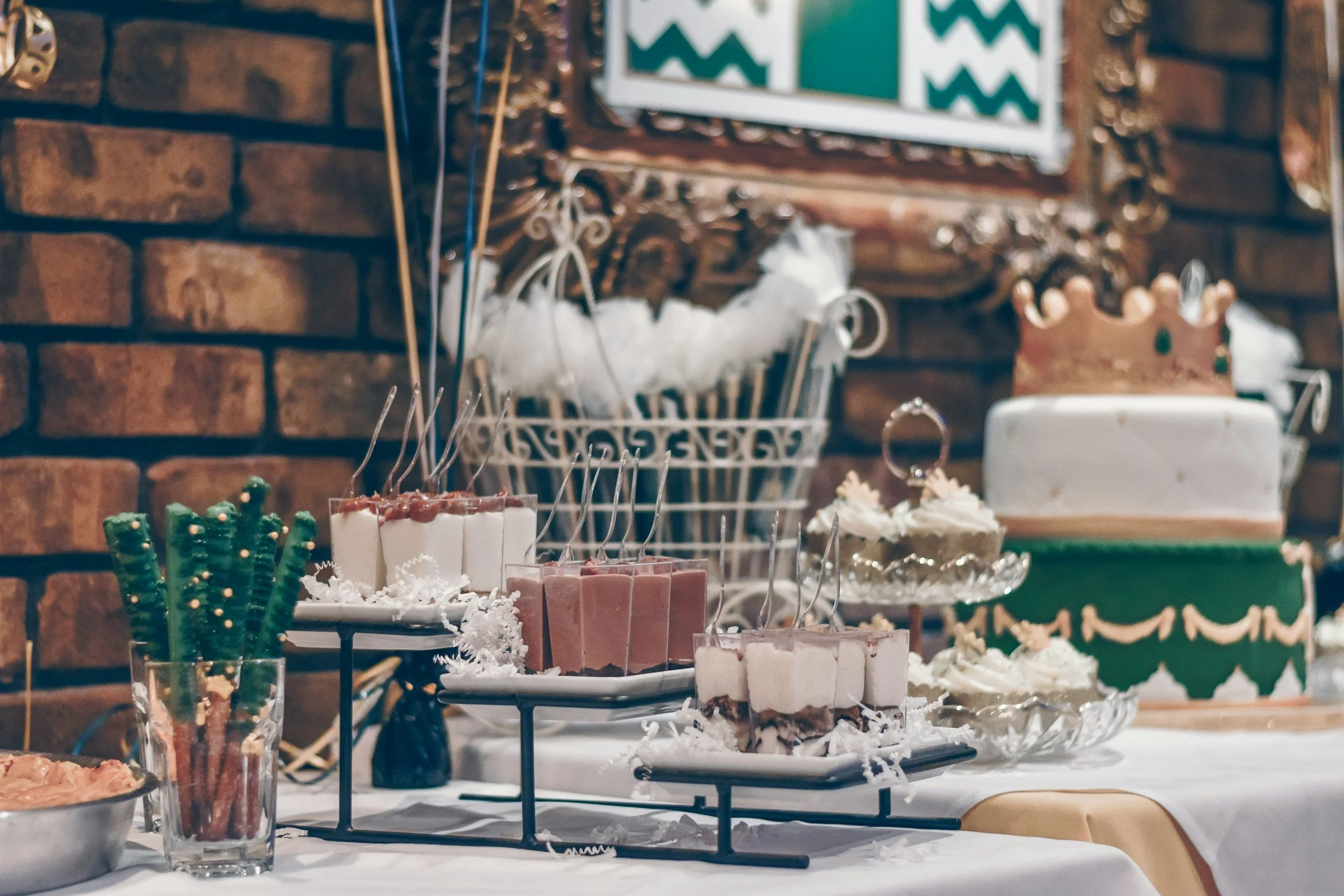 Decorated holiday dessert table with cakes, cupcakes, and treats, set against a brick wall.