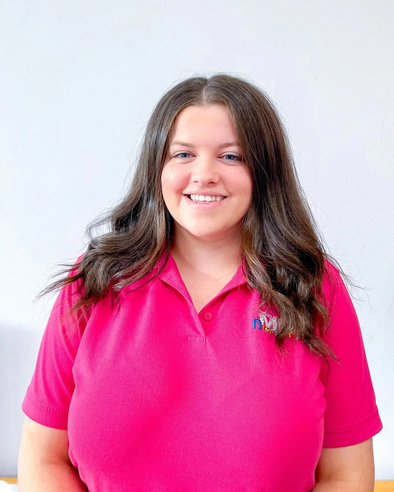A young woman with red hair, blue eyes, and a nose ring smiling and resting her hand on her head.