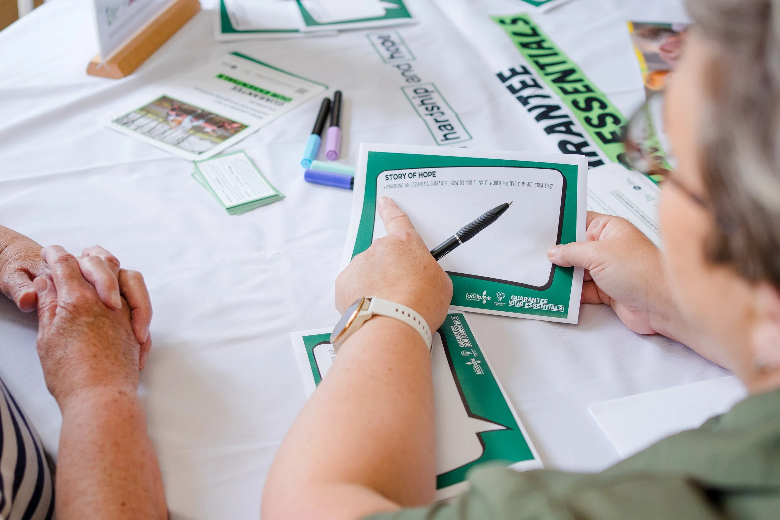 Person filling out a form titled 'Story of Hope' at a table with brochures, pens, and other materials related to a community or charity event.