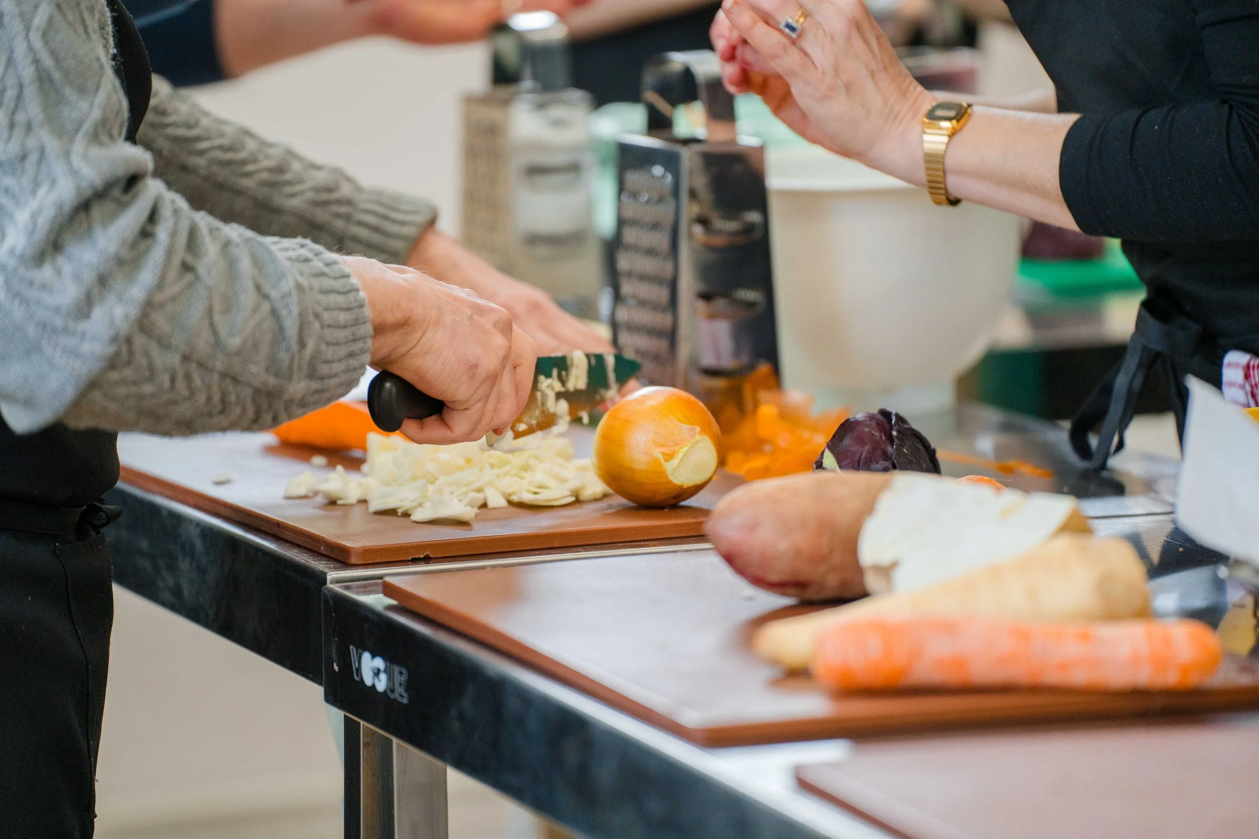Two people chopping onions and preparing vegetables on cutting boards in a kitchen.