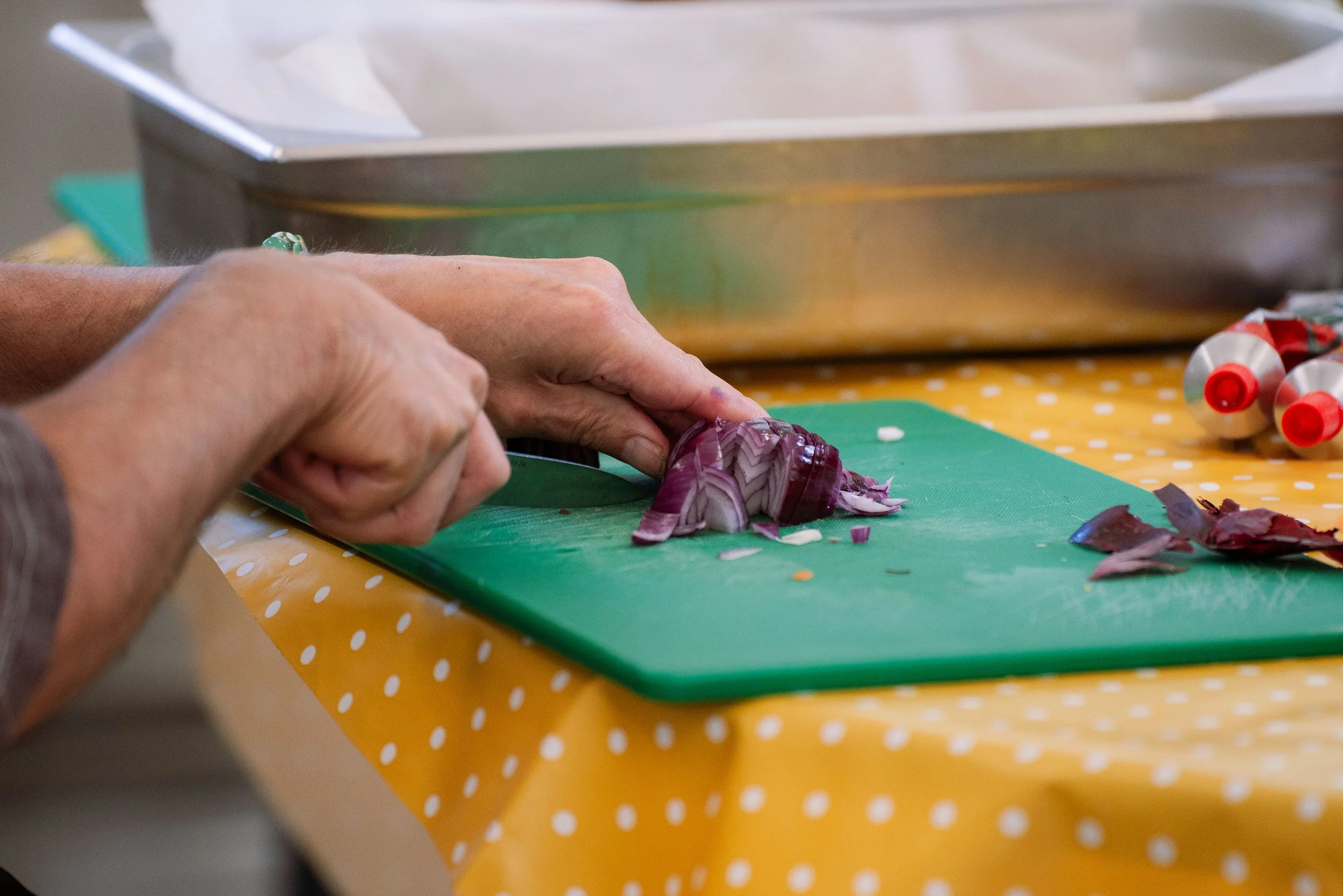 Person chopping purple onions on a green cutting board with a yellow polka dot tablecloth.
