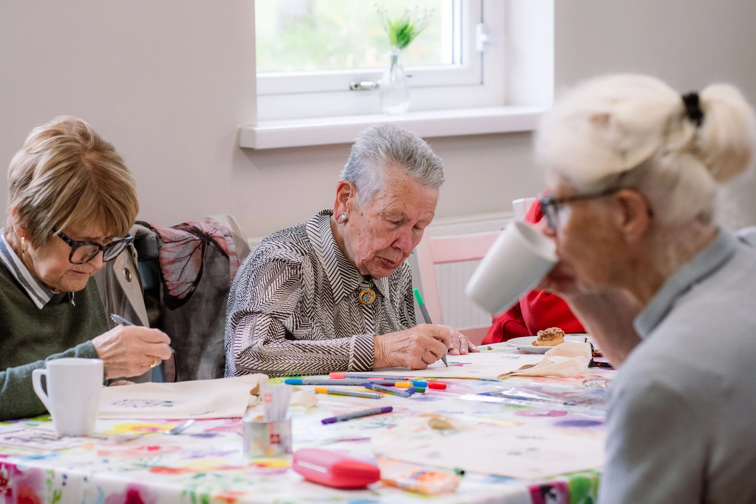 Elderly women sitting at a table engaging in arts and crafts, drawing with colored markers and pens.