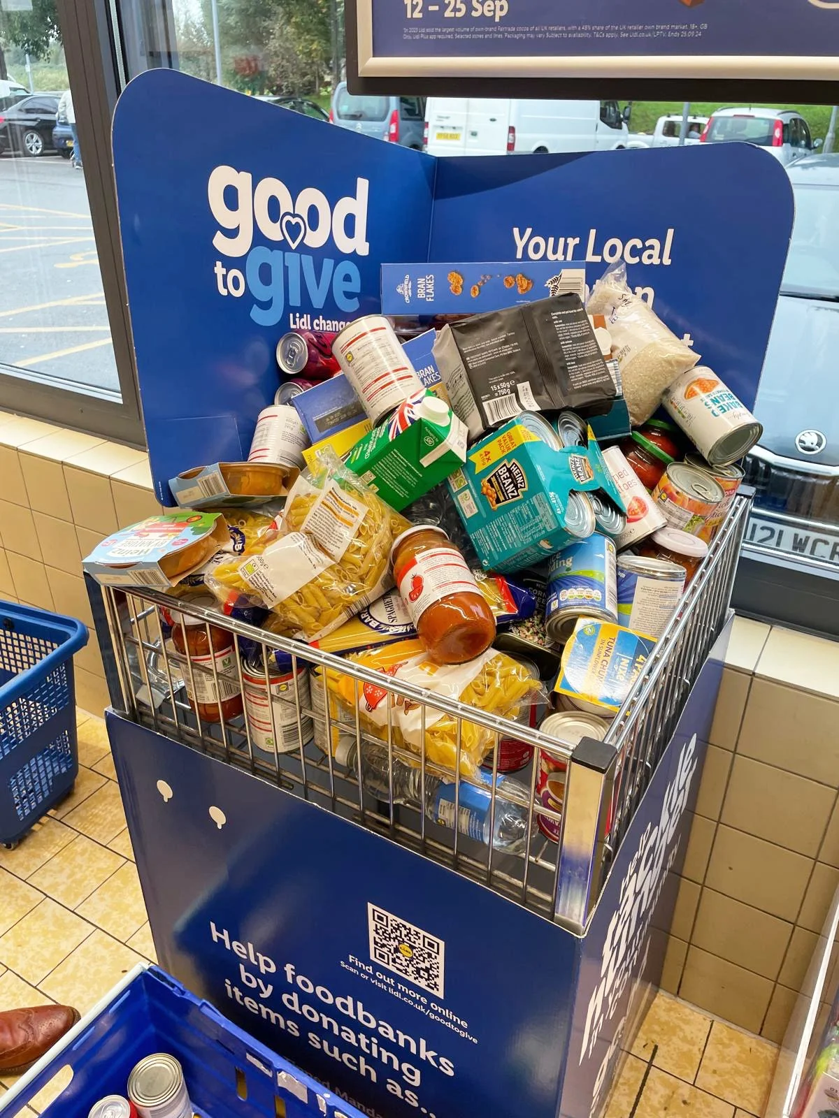 A donation bin filled with canned and packaged food items inside a store, with a sign indicating it's for food donations.