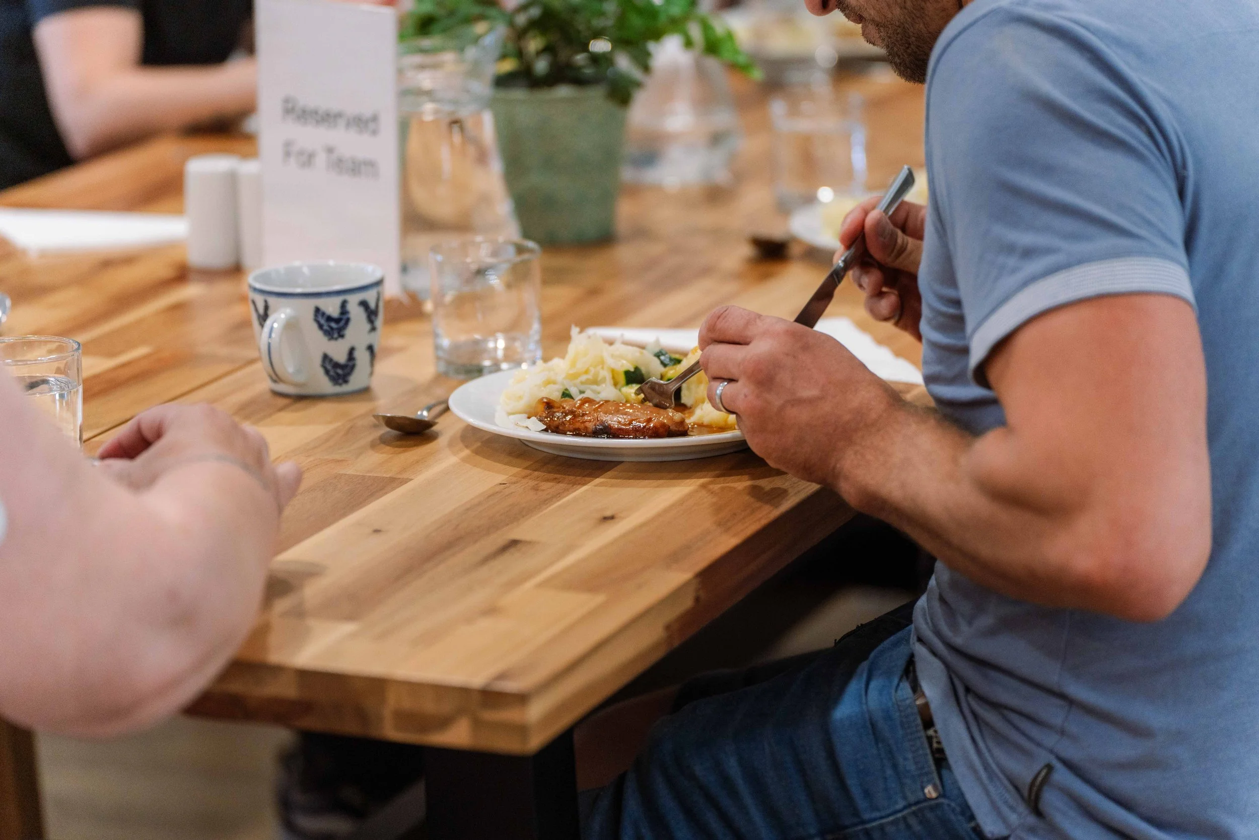 A person wearing a face mask and green sweater shopping in a grocery store aisle with shelves stocked with various packaged goods.