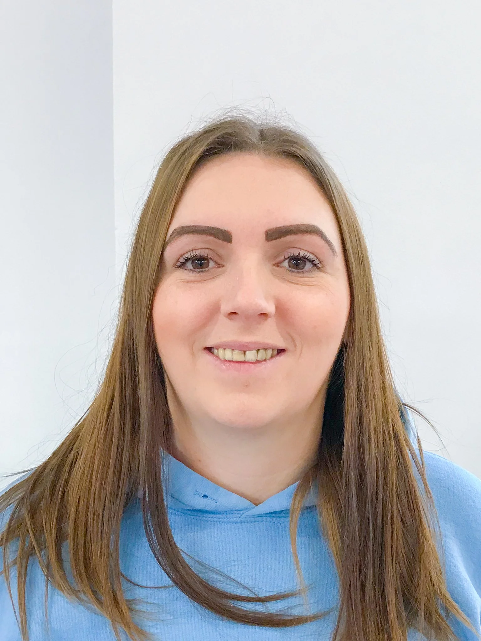 A young woman with long, blonde hair and blue eyes smiling at the camera, wearing a white and black striped shirt, standing in front of a colorful graffiti wall.